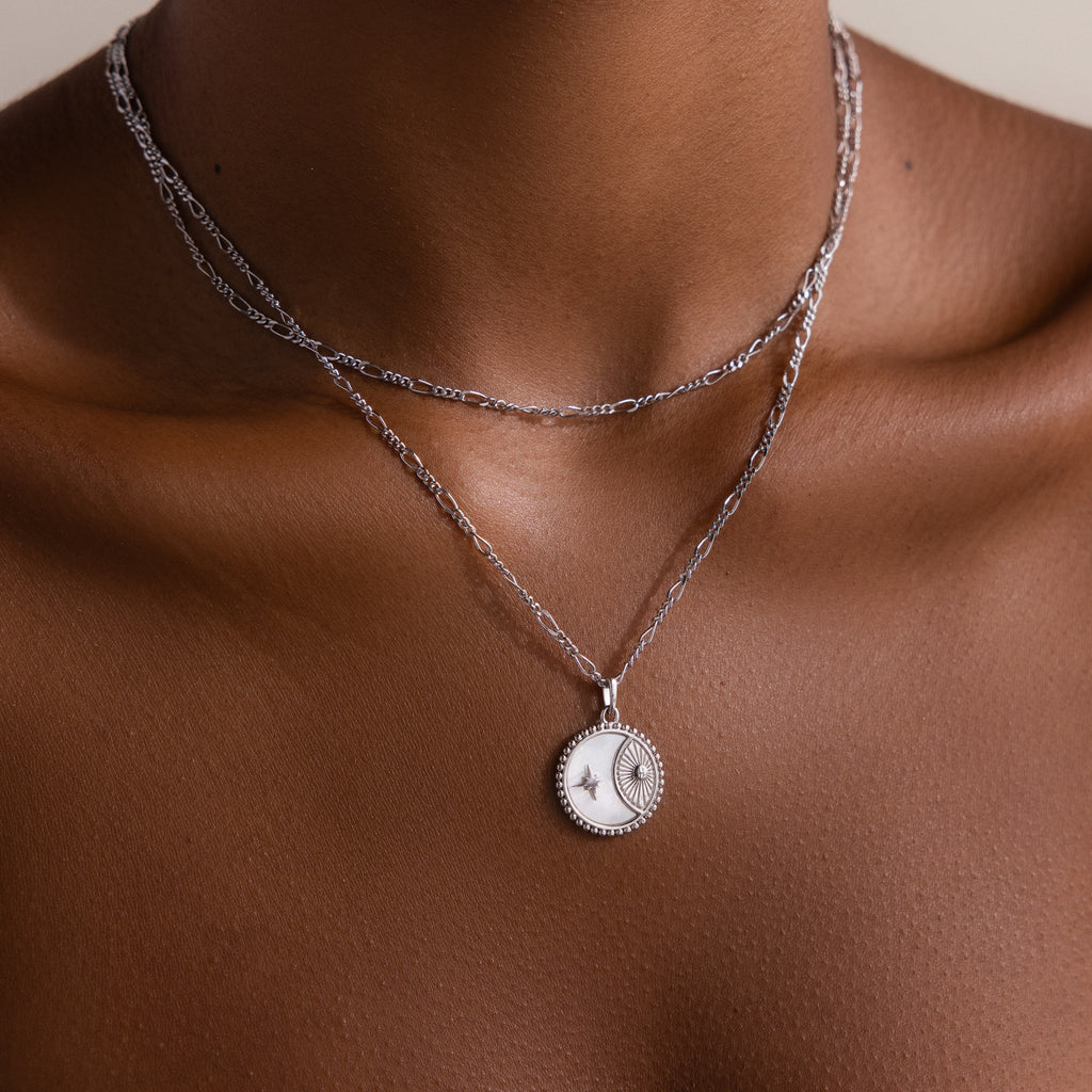 A person wearing two layered silver necklaces, one being the Gabi Coin Necklace in Silver with a vintage-inspired sun and moon pendant, shown against bare skin.