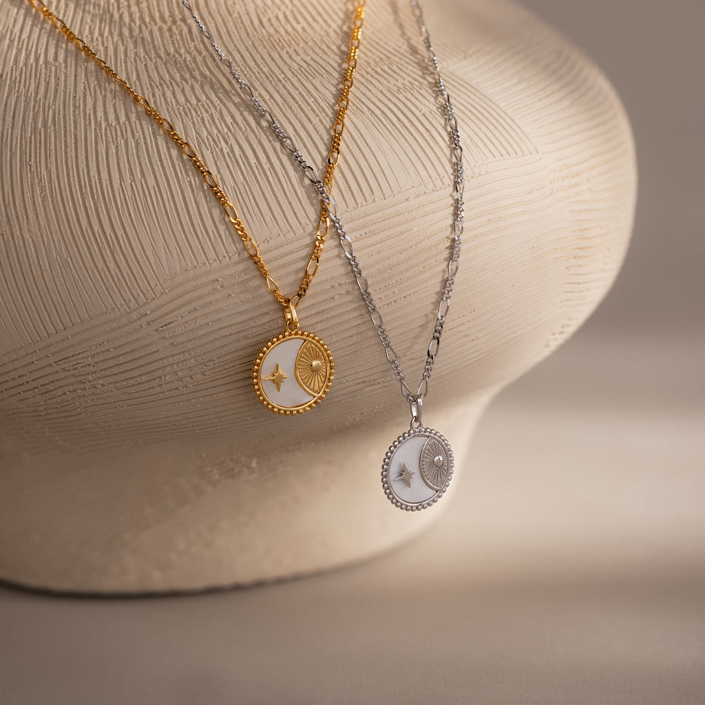 The Gabi Coin Necklaces in Silver and Gold are displayed on a textured, cream-colored vase—a perfect minimal jewelry accent for any style.