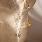 The Laura Starburst Duo Necklaces, featured in gold and silver with starbursts and diamond accents, are displayed on a beige textured surface—ideal for creating a chic layered look.