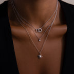 A person wears three layered silver necklaces, featuring the Sun  Moon Eternity Necklace, a celestial circle necklace, and a starburst pendant.