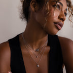 Woman in a black top wears layered silver celestial necklaces, including the Sun  Moon Eternity Necklace in Silver, while looking off to the side against a neutral background.