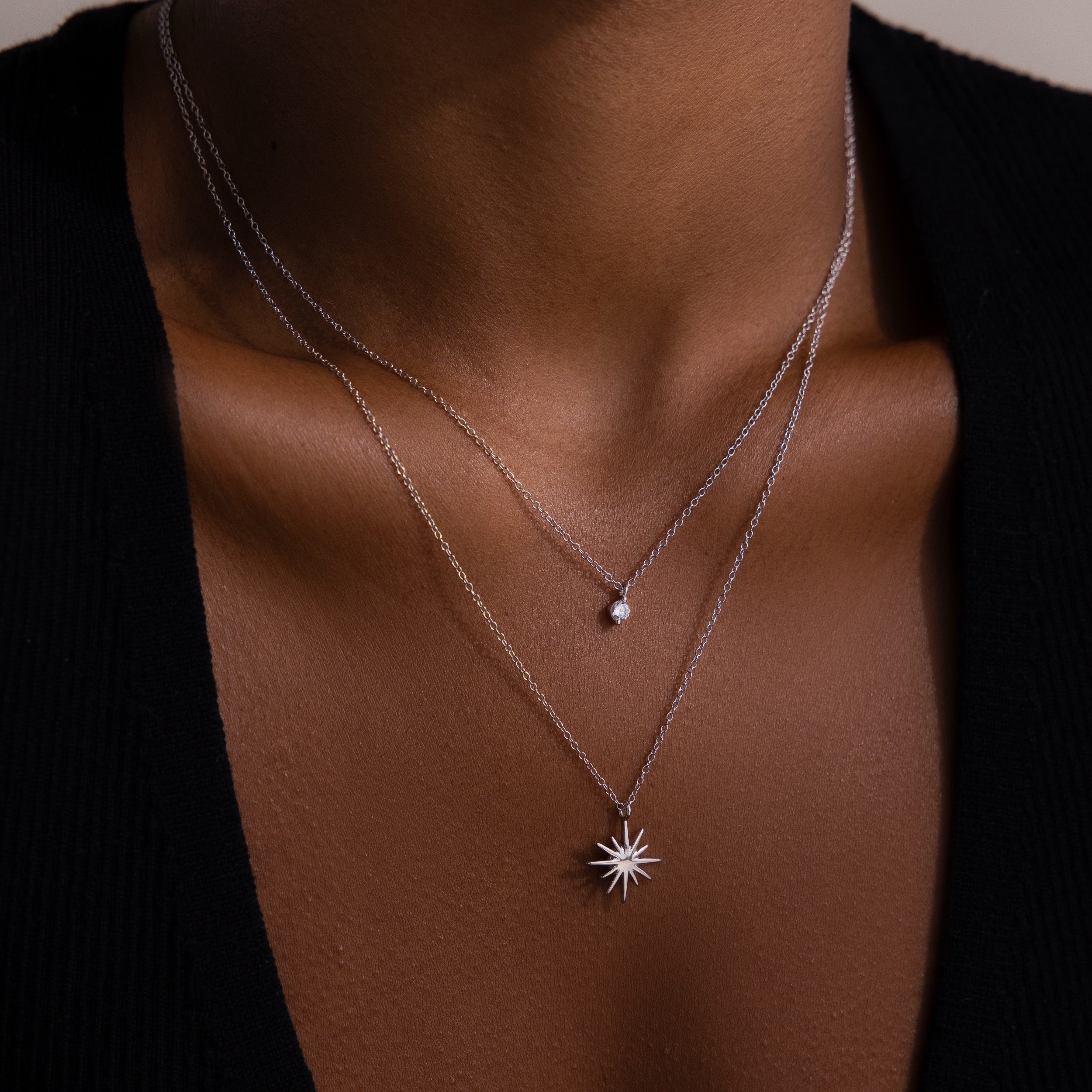 Close-up of a woman’s neck wearing the Laura Starburst Duo Necklace in Silver—two chains, one with a diamond accent and the other with a striking starburst pendant.