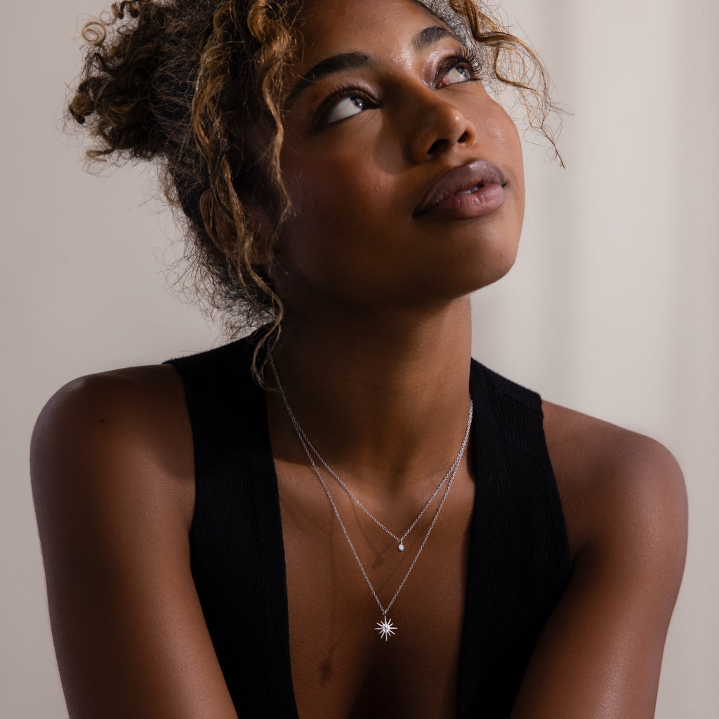 A woman with curly hair wears the Laura Starburst Duo Necklace in Silver and a black sleeveless top, looking up against a neutral background.