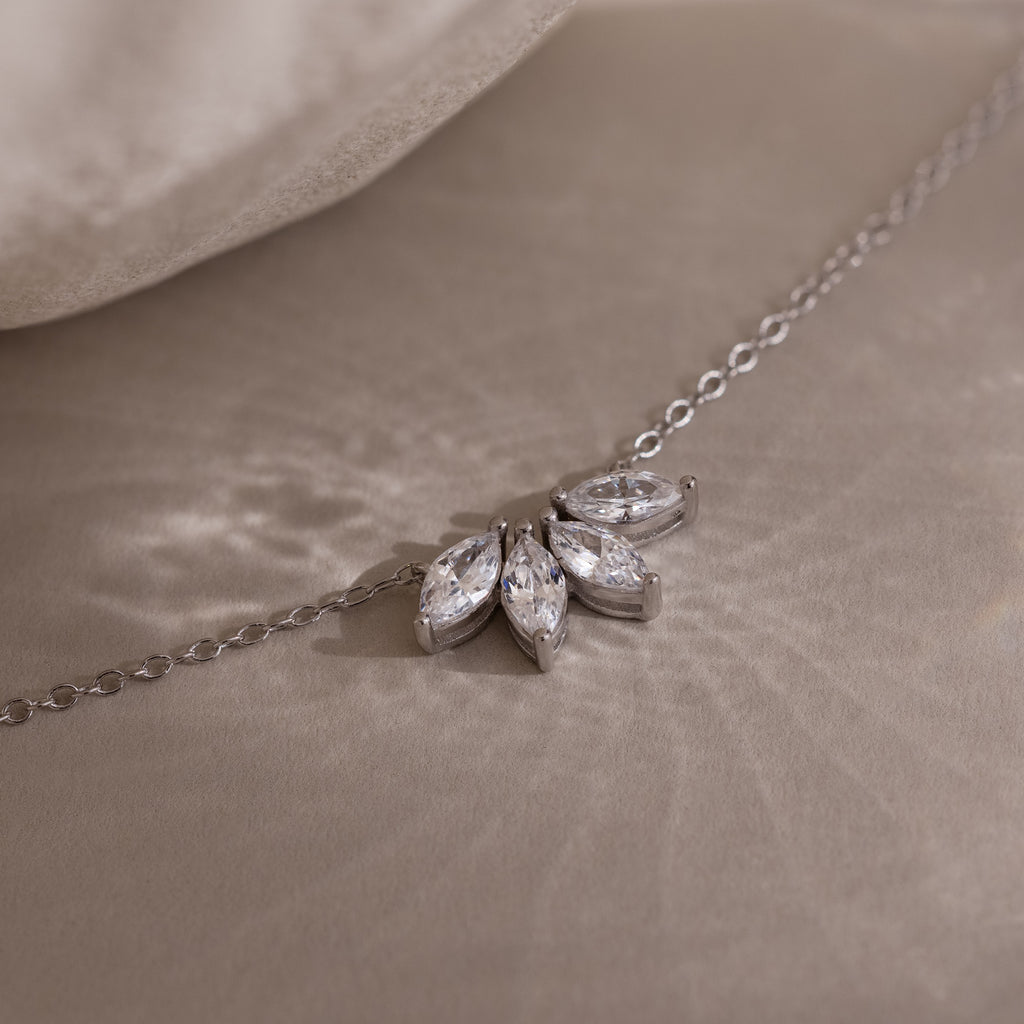 The Marquise Diamond Necklace in Silver, featuring three marquise-cut diamonds arranged in a floral design, rests elegantly on a soft beige surface.