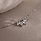The Marquise Diamond Necklace in Silver, featuring three marquise-cut diamonds arranged in a floral design, rests elegantly on a soft beige surface.