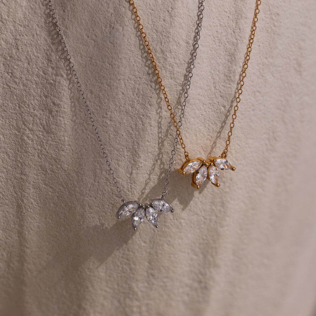 Two Marquise Diamond Necklaces in silver and gold, each featuring a floral-inspired, leaf-shaped diamond pendant, displayed against a textured background.