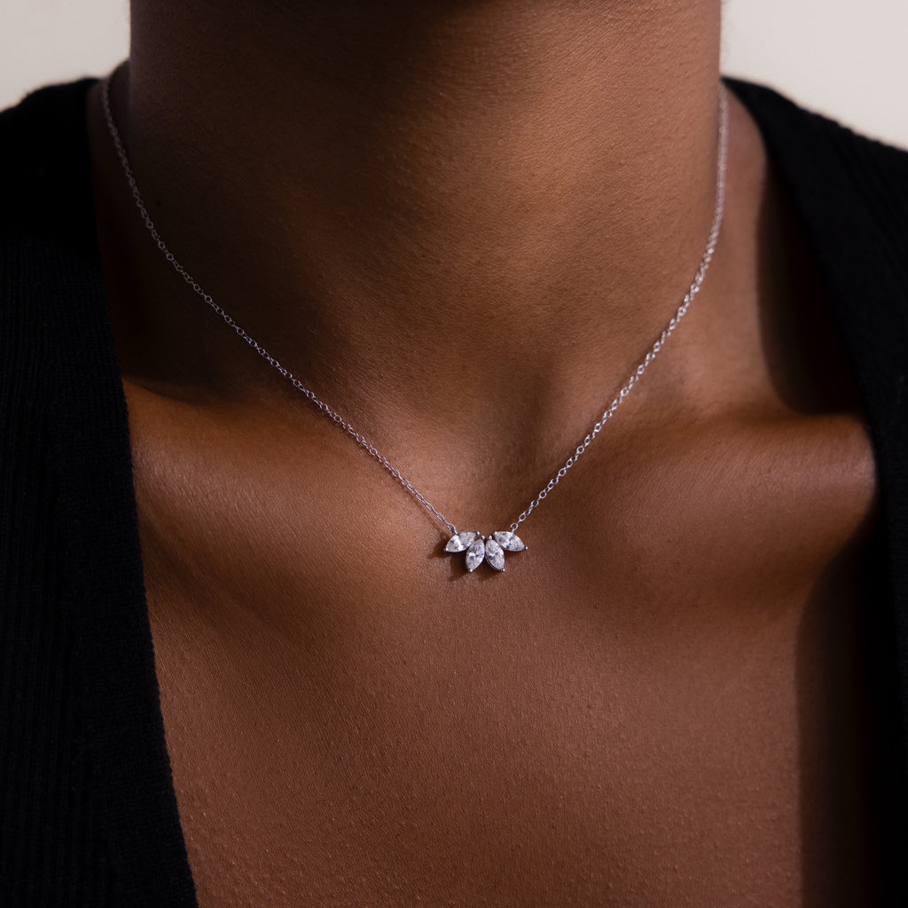 The Marquise Diamond Necklace in Silver, featuring three leaf-shaped pendants, sparkles beautifully against a dark top when worn around the neck.