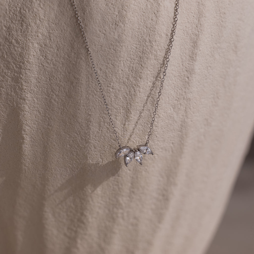 The Marquise Diamond Necklace in Silver features three leaf-shaped gemstones, embodying the elegance of fine diamond jewelry against a light textured fabric.