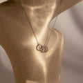 The Sun  Moon Eternity Necklace in Silver features intertwined sun and moon pendants, elegantly displayed on a beige textured mannequin—perfect for any occasion.
