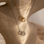 The Sun Moon Eternity Necklace, shown in Gold and Silver features two intertwined pendants on a textured beige stand—a stunning celestial piece for any jewelry collection.
