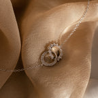 The Sun  Moon Eternity Necklace, featuring a celestial pendant, is displayed on a soft beige fabric background.