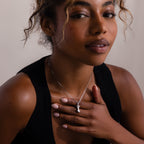 A woman in a black top touches her chest, confidently showcasing the elegant Kinn Body Necklace in Silver as she looks at the camera.