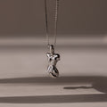 The Kinn Body Necklace in Silver features an abstract pendant on a delicate chain, casting a soft shadow—an elegant and empowering accessory inspired by the Venus de Milo.
