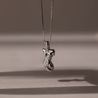 The Kinn Body Necklace in Silver features an abstract pendant on a delicate chain, casting a soft shadow—an elegant and empowering accessory inspired by the Venus de Milo.
