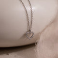 The Forever Pave Heart Necklace features a diamond-studded heart pendant, making it ideal bridal jewelry, beautifully showcased on a soft, light fabric background.