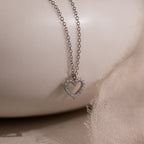 The Forever Pave Heart Necklace features a diamond-studded heart pendant, making it ideal bridal jewelry, beautifully showcased on a soft, light fabric background.