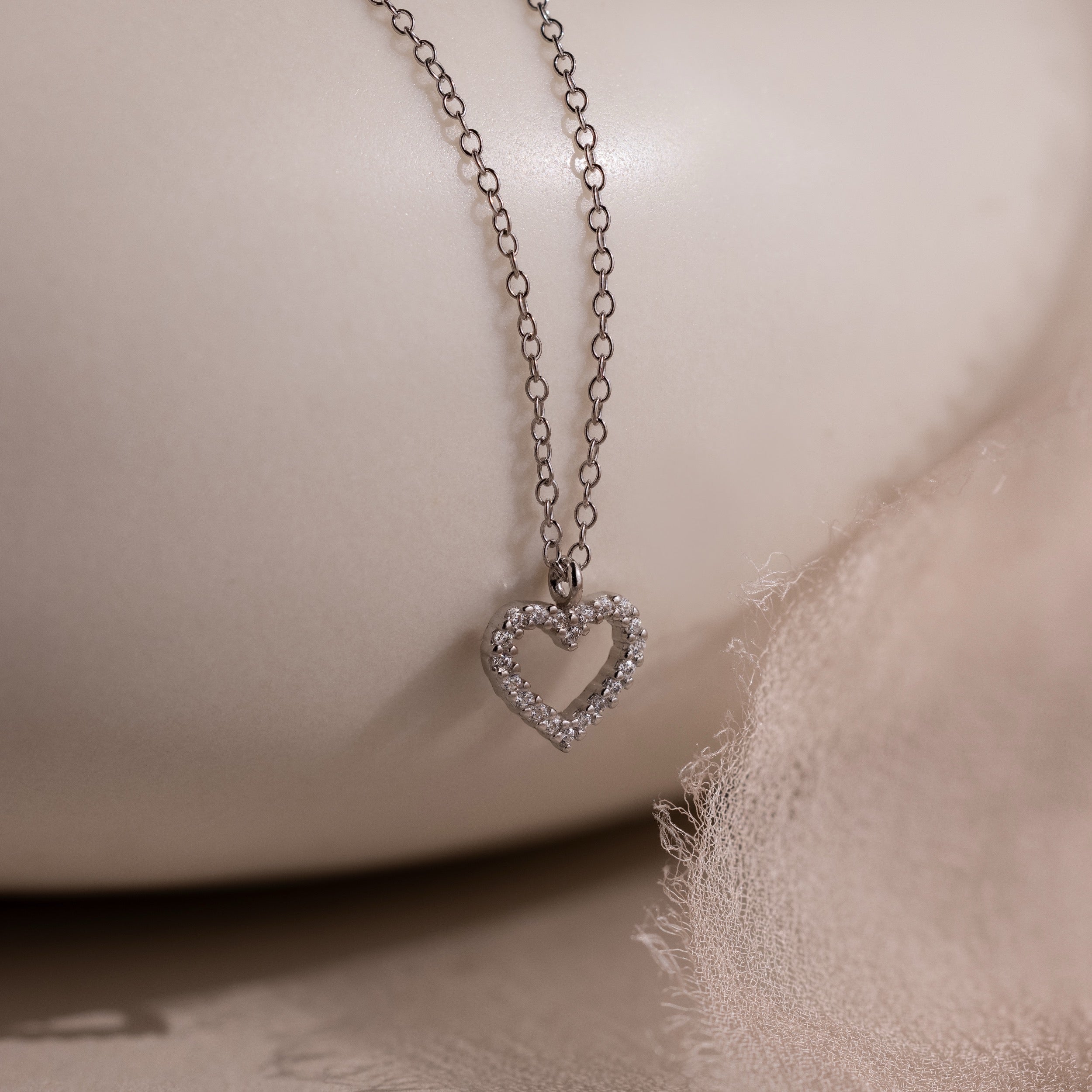 The Forever Pave Heart Necklace features a diamond-studded heart pendant, making it ideal bridal jewelry, beautifully showcased on a soft, light fabric background.