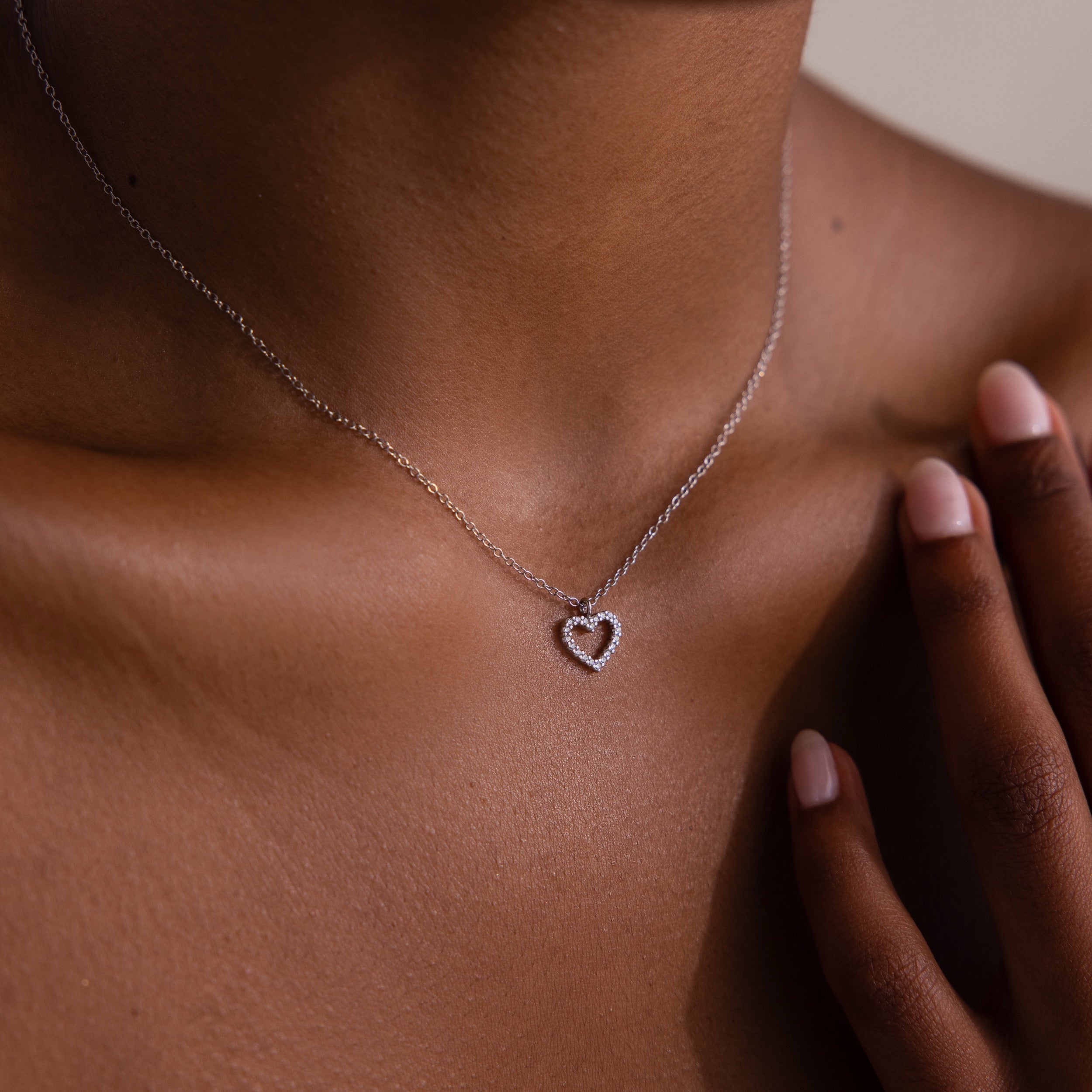 A close-up of a woman wearing the Forever Pave Heart Necklace in Silver, her hand gently touching her neck.