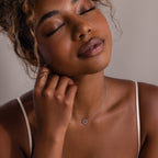 Woman with curly hair, eyes closed, gently touches her neck while wearing the Forever Pave Heart Necklace in Silver and a beige top.