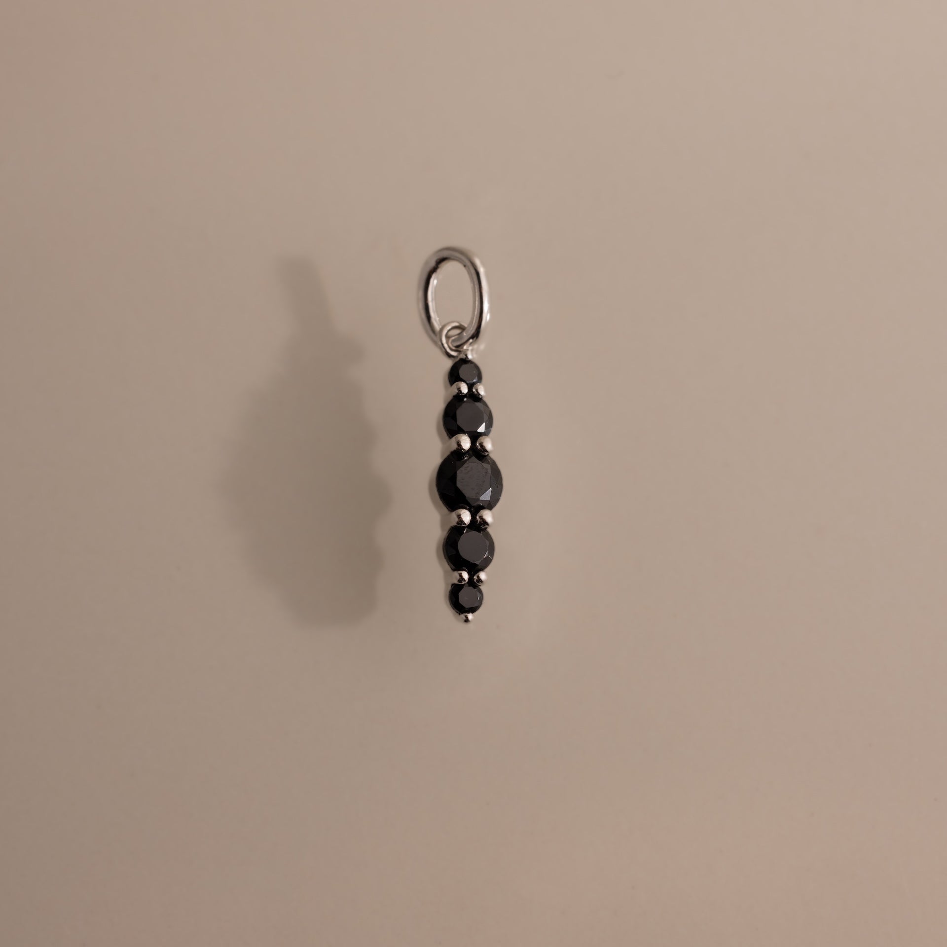 The Ombre Lace Onyx Charm is a silver pendant featuring a vertical row of five black beads, shown against a plain beige background.