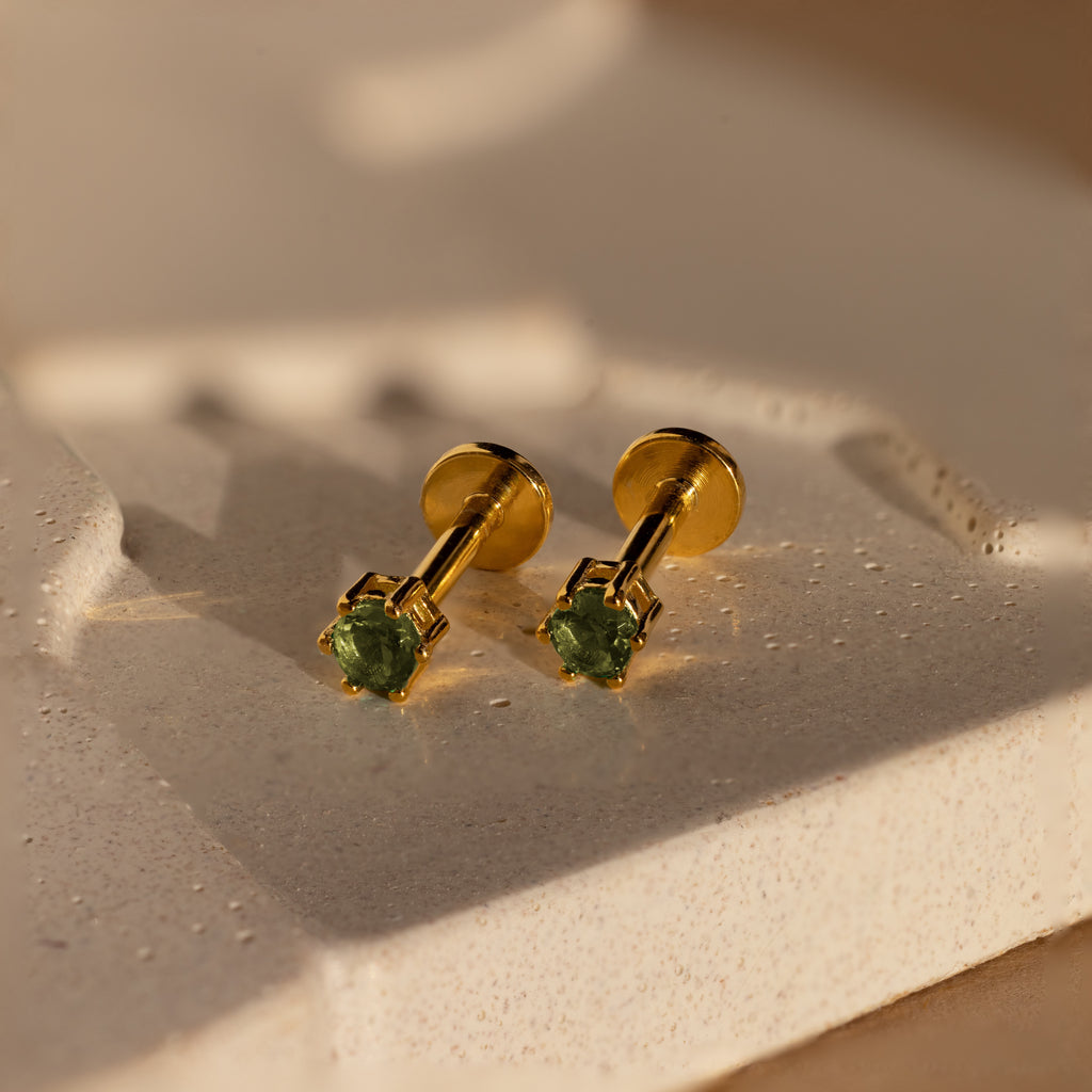 Peridot Flatback Studs with green gemstones, ideal as birthstone jewelry, are displayed on a textured, light-toned surface under warm lighting.