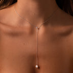 Close-up of a woman's neck adorned with the Pearl Drop Lariat Necklace in Sterling Silver, featuring a delicate vertical chain and subtle pearl pendant—an elegant jewelry piece.