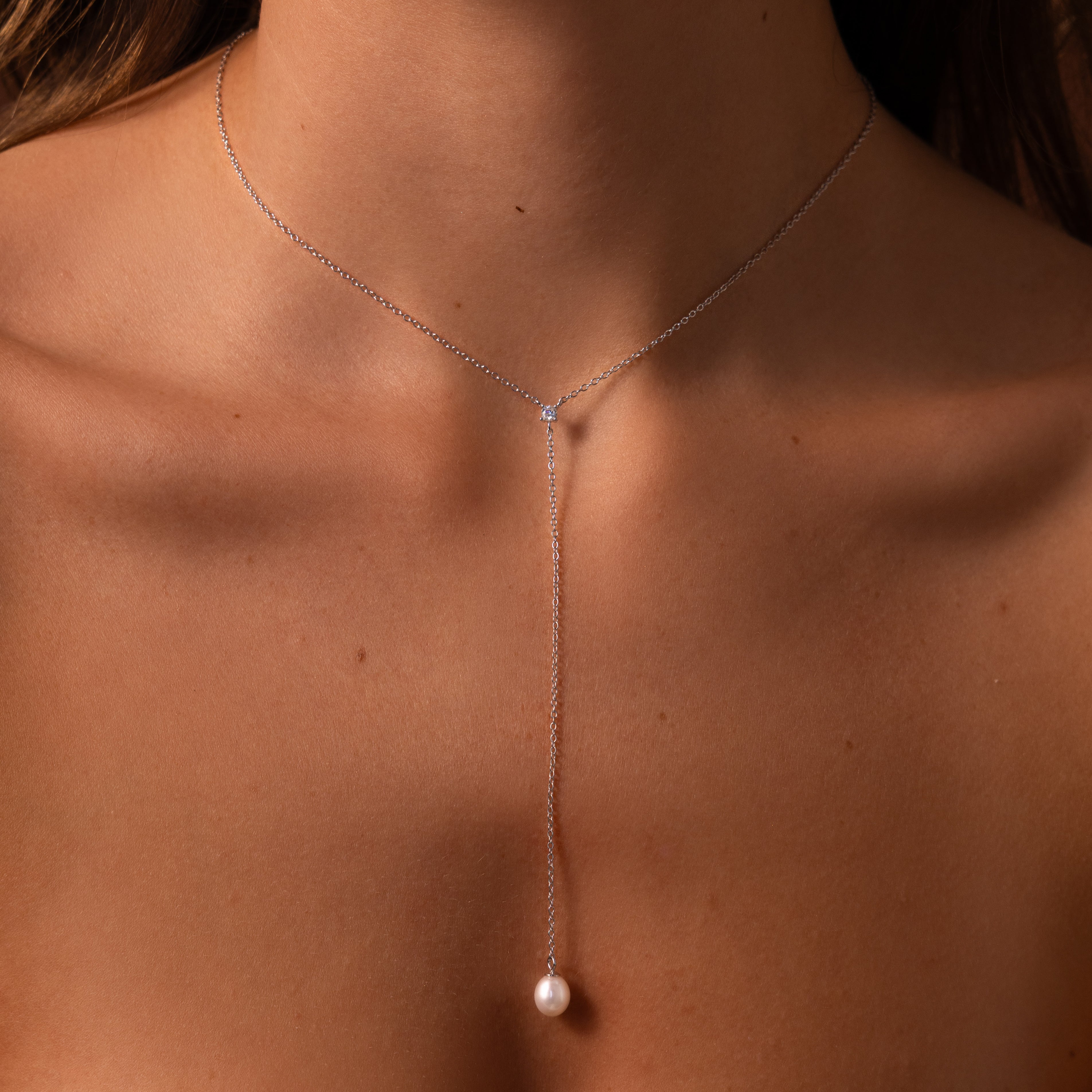 Close-up of a woman's neck adorned with the Pearl Drop Lariat Necklace in Sterling Silver, featuring a delicate vertical chain and subtle pearl pendant—an elegant jewelry piece.