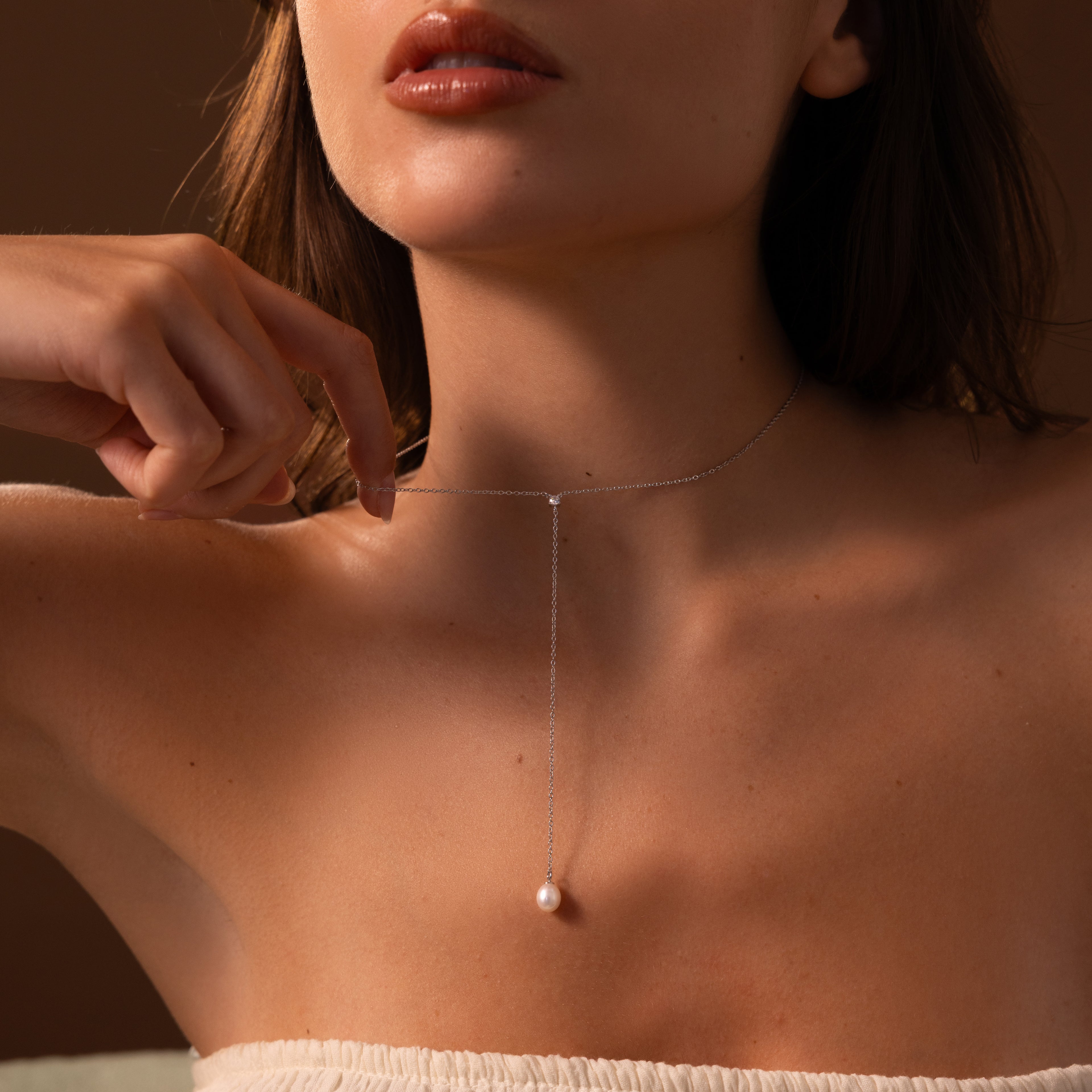A woman wears the Pearl Drop Lariat Necklace in Sterling Silver—a delicate vertical chain featuring a single pearl pendant—against bare skin.