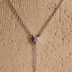 The Pearl Drop Lariat Necklace in Sterling Silver features a delicate vertical chain with a single pearl pendant, elegantly displayed against a textured beige background—an ideal choice for lovers of refined jewelry.