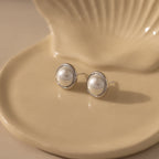 The Pearl Bezel Studs in Sterling Silver are displayed elegantly on a cream-colored, shell-shaped dish.