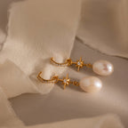 The North Star Pearl Hoops in 18K Gold, featuring star accents, pearls, and small diamonds, are displayed on soft beige fabric—a stunning celestial-inspired jewelry piece.