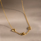 Up close of a gold dainty bubble initial charm necklace with letters "AHR" resting on a neutral background.