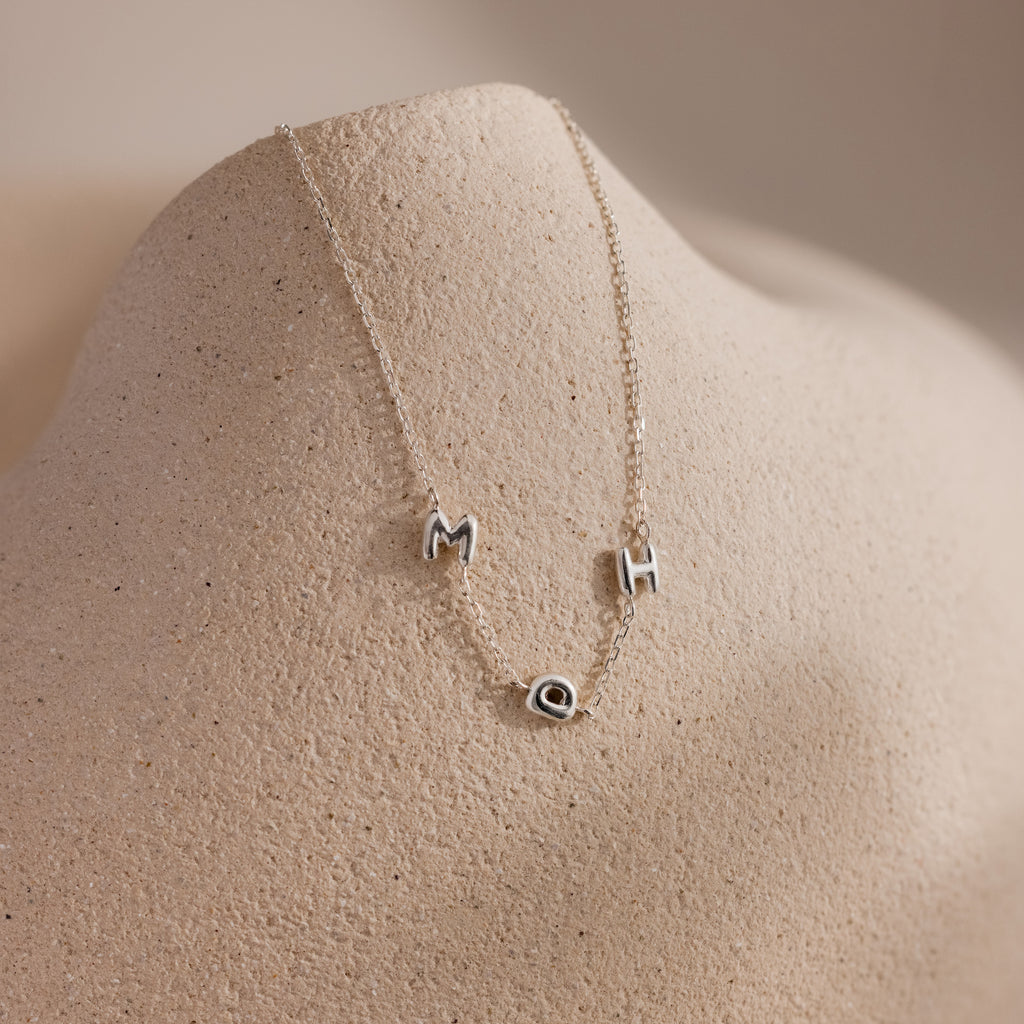 Dainty silver bubble letter necklace with the initials "MDH" displayed on a neutral surface.