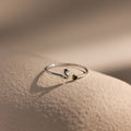 Up close of a silver bubble letter duo gemstone ring with the initial "S" and a green peridot birthstone resting on a neutral surface.