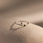 Up close of a silver bubble letter duo gemstone ring with the initial "S" and a green peridot birthstone resting on a neutral surface.