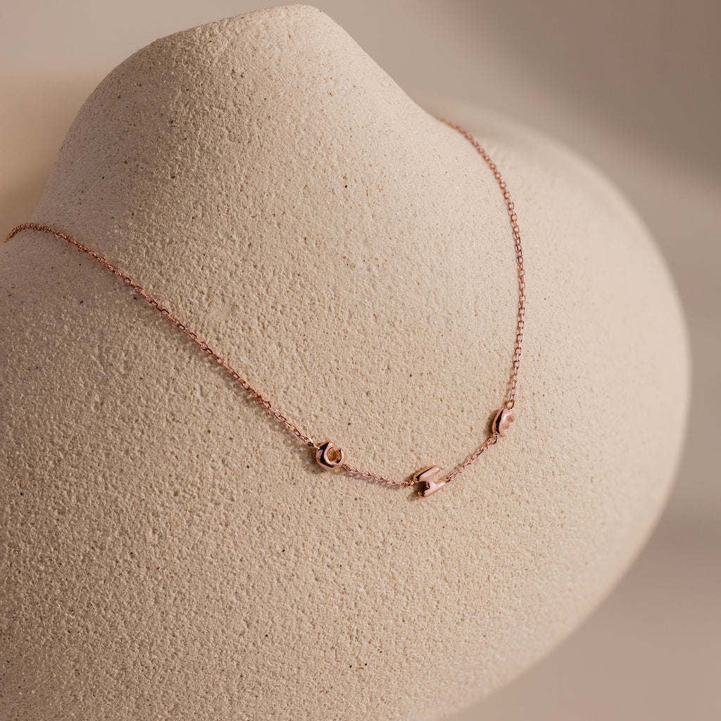 Rose gold dainty bubble initial necklace with the letters "CHE" against a neutral display.