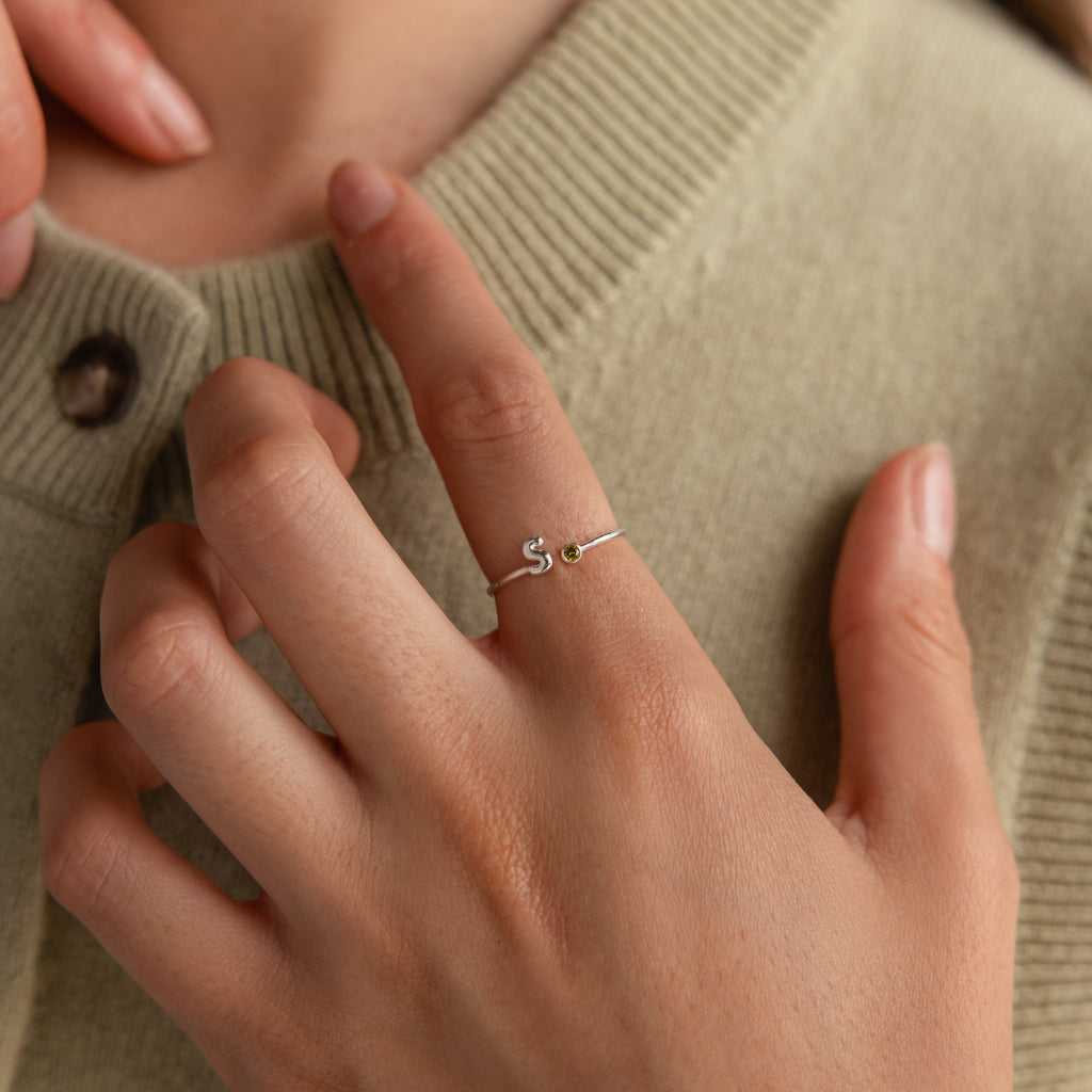 Up close of model wearing a dainty silver bubble letter gemstone ring with the initial "S" and a green peridot birthstone.