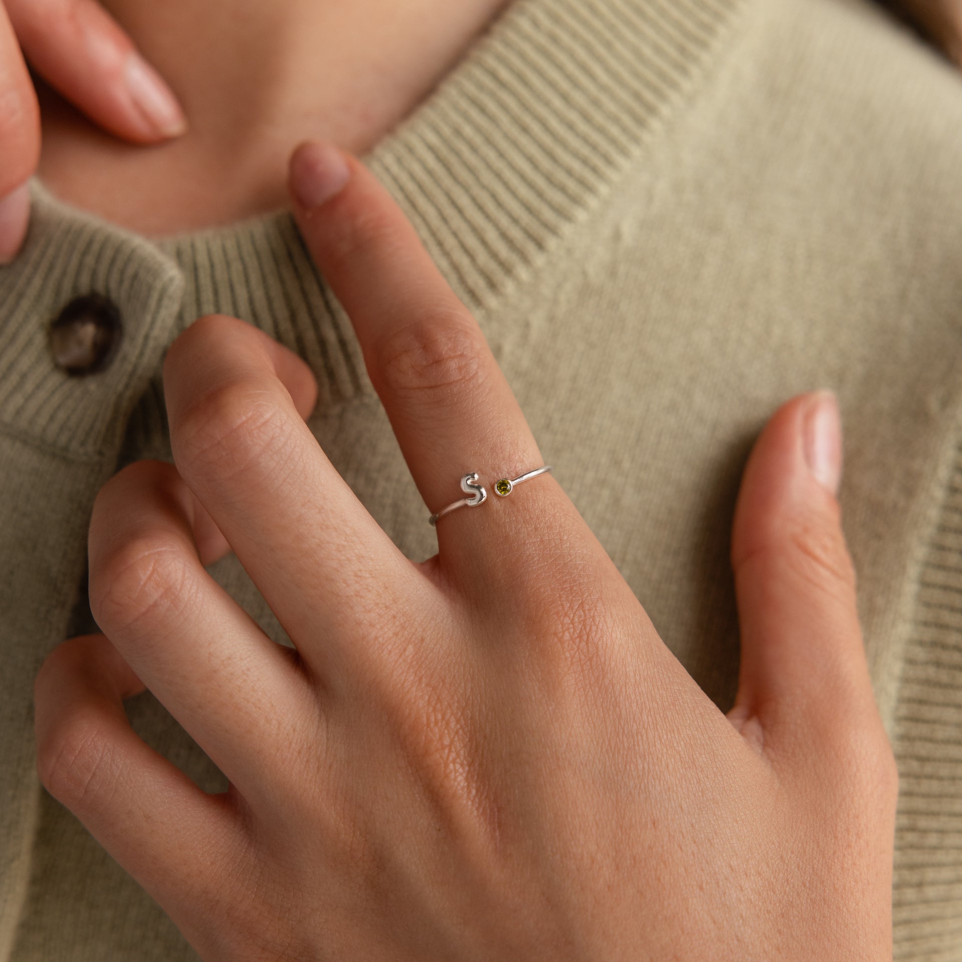 Up close of model wearing a dainty silver bubble letter gemstone ring with the initial "S" and a green peridot birthstone.