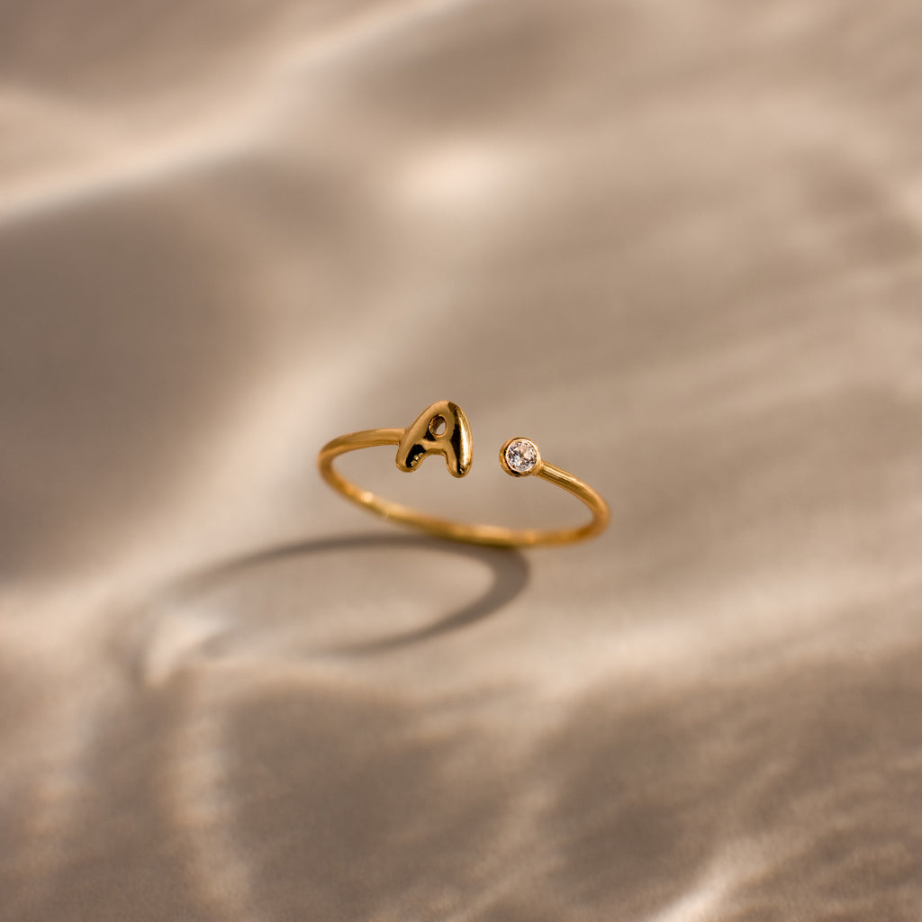 Up close of a dainty gold bubble letter gemstone duo ring with the initial "A" and a clear diamond birthstone.