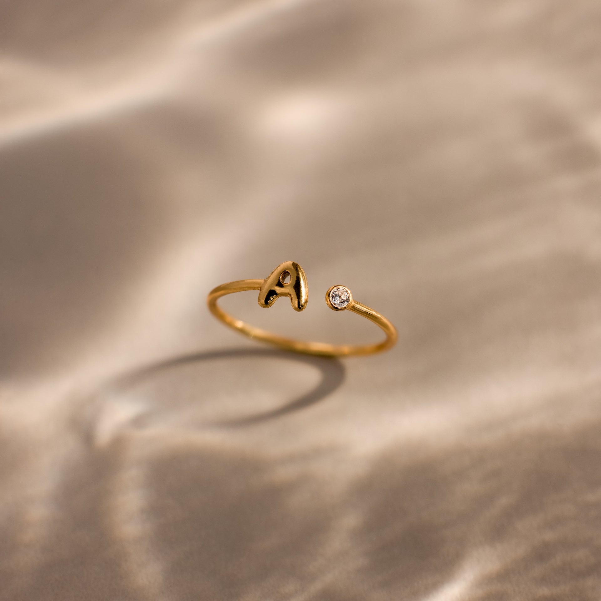 Up close of a dainty gold bubble letter gemstone duo ring with the initial "A" and a clear diamond birthstone.