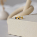 Square Bezel Sapphire Flatback Studs showcasing small sapphire CZ gemstones in gold, elegantly presented on a cream-colored textured surface.