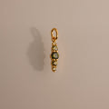 The Ombre Lace Peridot Charm is a gold pendant featuring four small gemstones arranged vertically, adding a personalized touch against a neutral background.