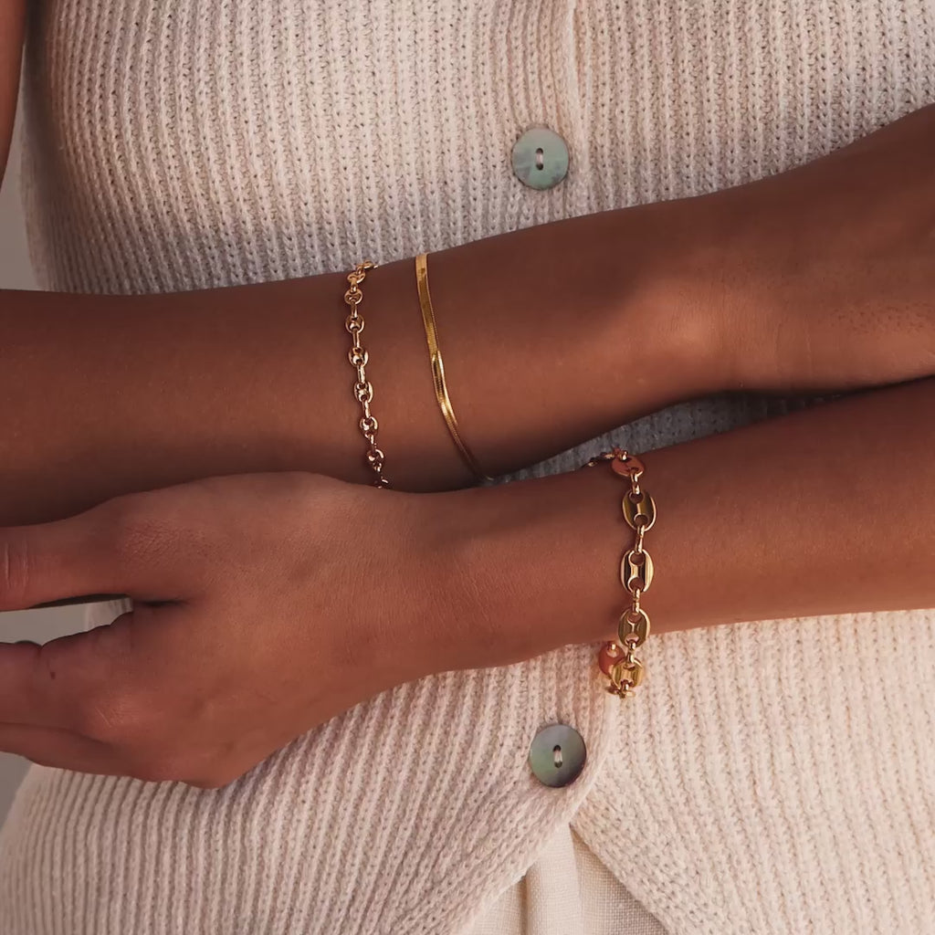 Model showcasing the Mini Mariner Chain Bracelet in gold, stacked with a larger mariner chain bracelet and a herringbone bracelet.