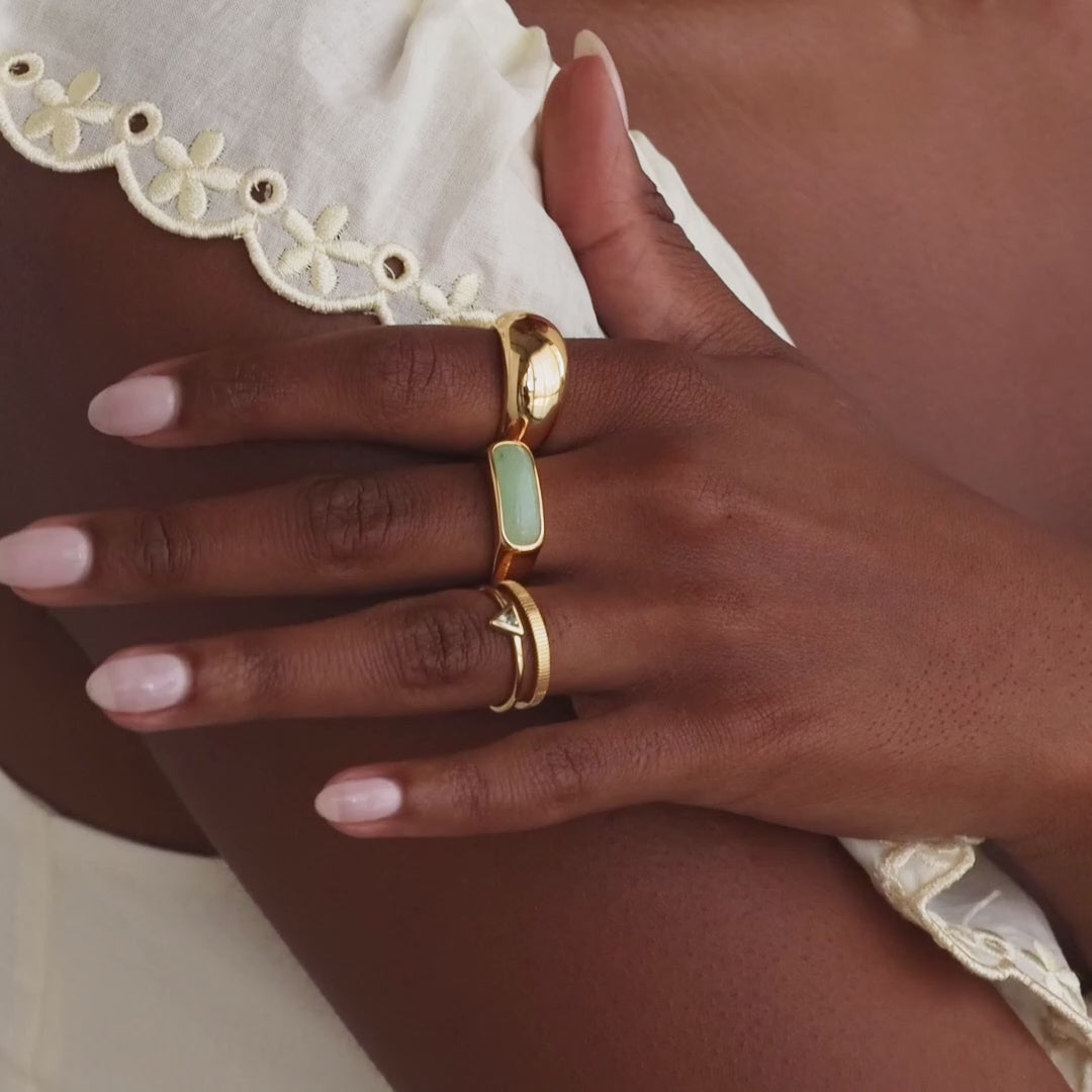 Model showcasing a gold signet ring with a polished green jade gemstone inlay, stacked with multiple gold rings.