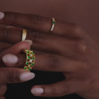 Model showcasing a gold checkered band ring featuring alternating rows of emerald and diamond round-cut CZ stones set in an openwork grid design, stacked with multiple gold rings.