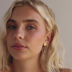 Model showcasing a gold heart-shaped initial stud earring with pave crystals, styled with multiple gold and crystal hoops.