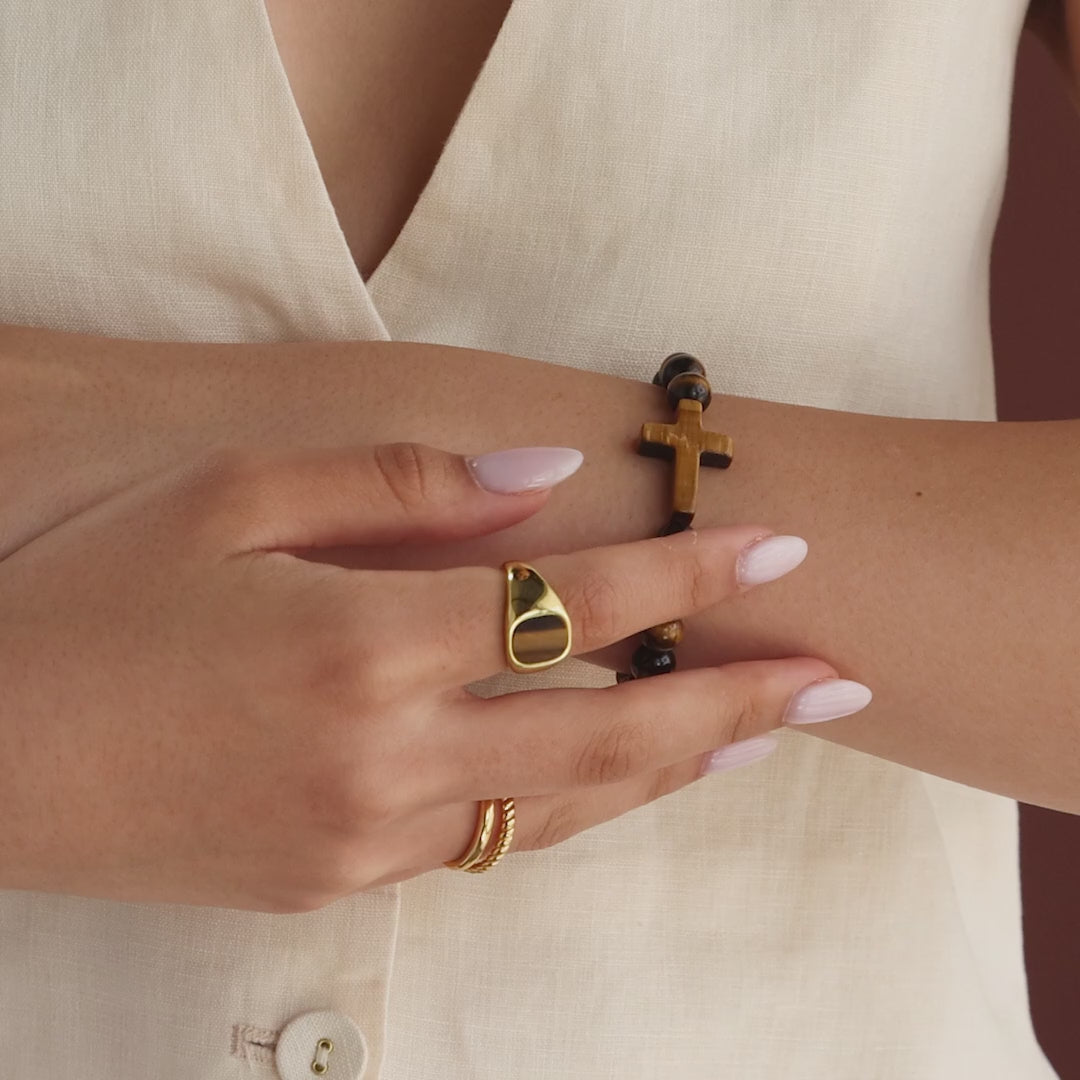 Model showcasing the Tigers Eye Cross Bracelet, styled with a gold tigers eye signet ring and gold duo band ring.