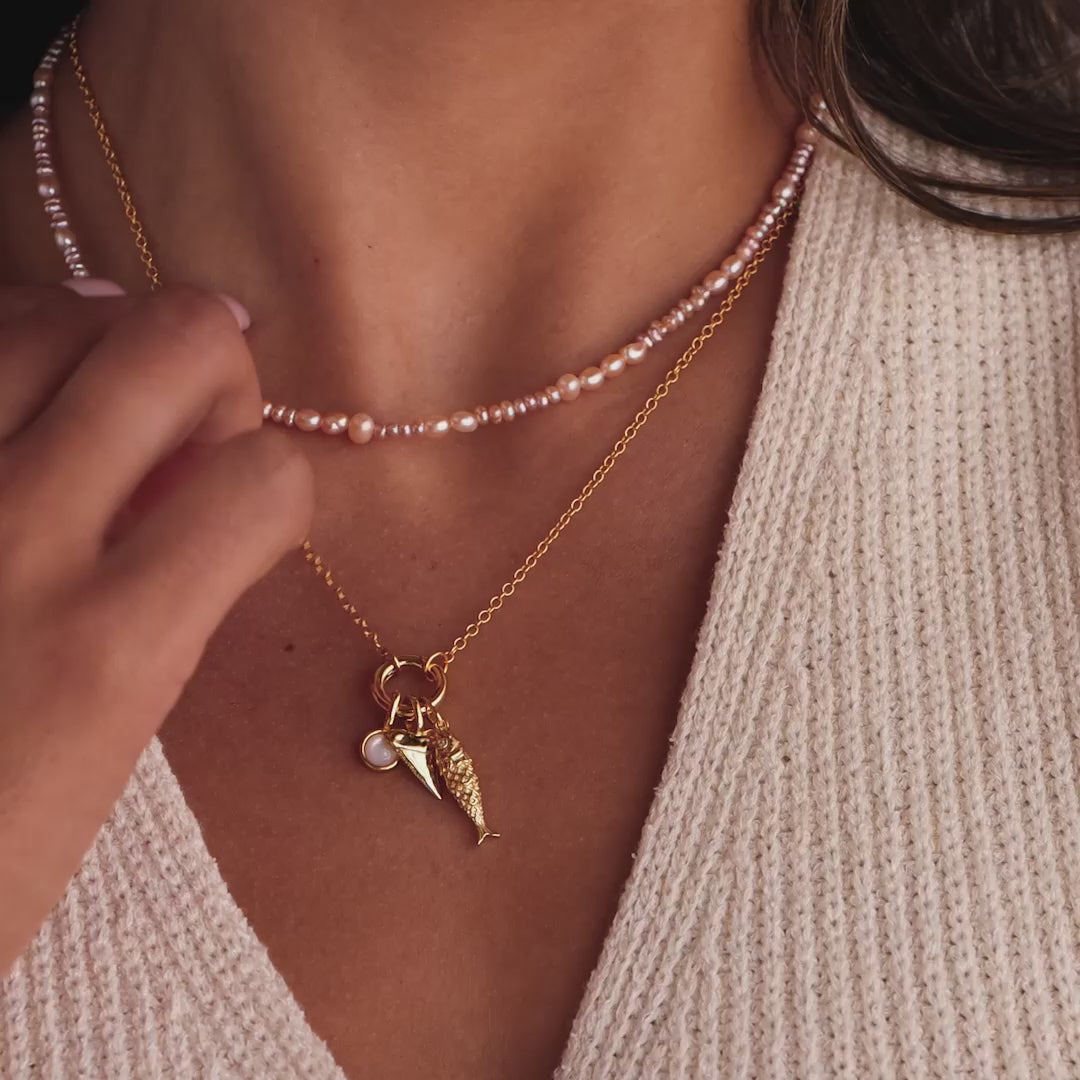 Model showcasing the Fish Charm on a chain necklace, paired with a pearl charm and a shark tooth charm, styled with a pink freshwater pearl choker.