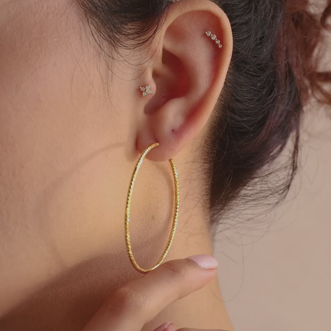 Model wearing a statement gold hoop earring with a twisted texture, complemented by dainty gemstone studs along the ear.
