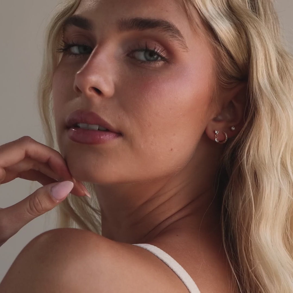 Model showcasing gold Heart Drop Flat Back earrings alongside a pave diamond huggie and a single diamond stud, showcasing a stacked look